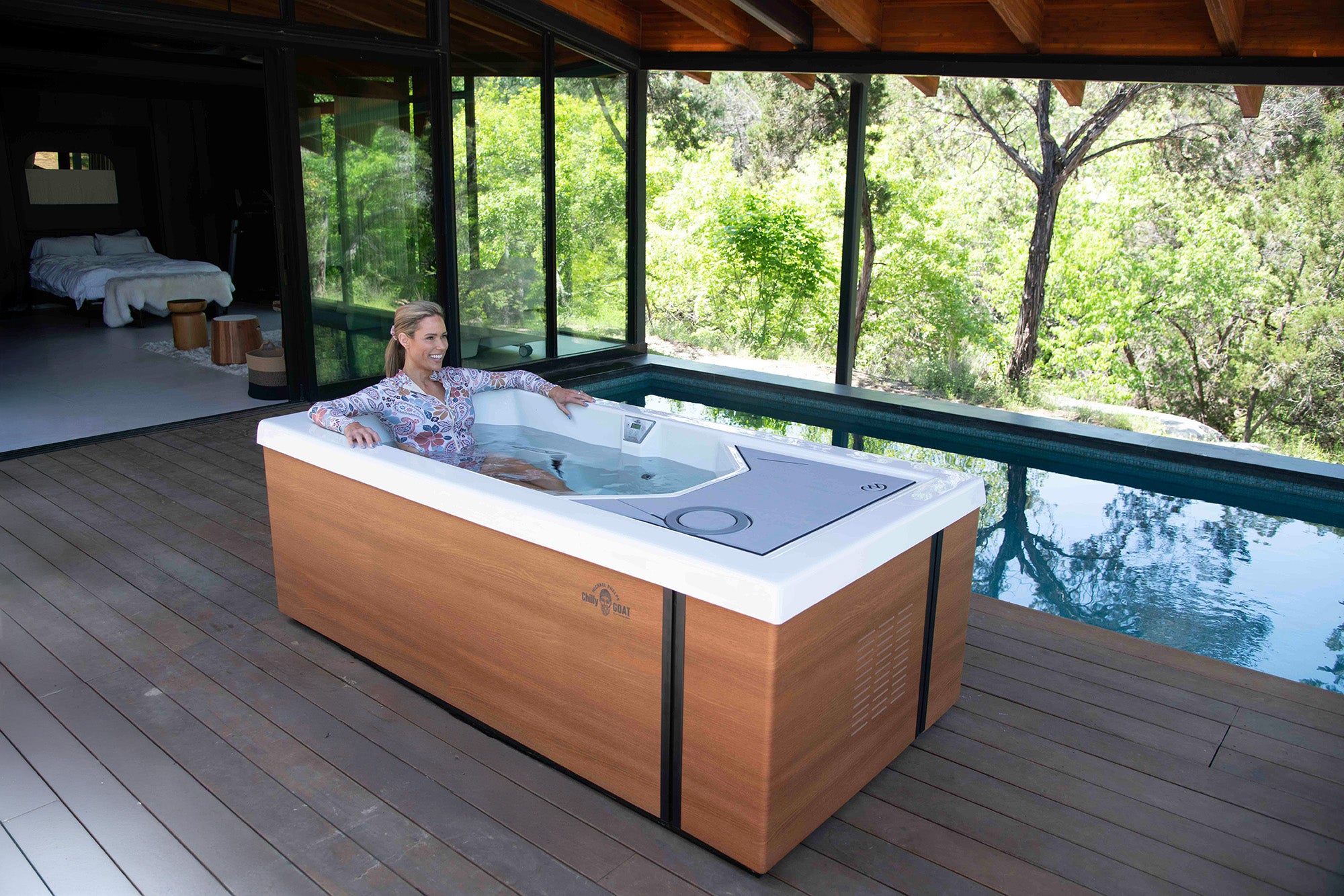 Person relaxing in a hot tub on a deck with a forest view.