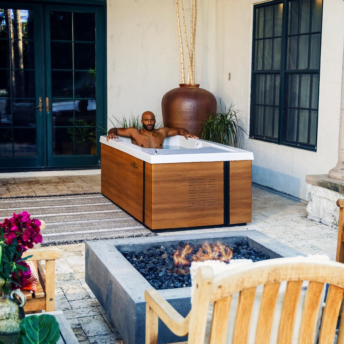 Man sits in cold tub on a patio in front of a a fire place
