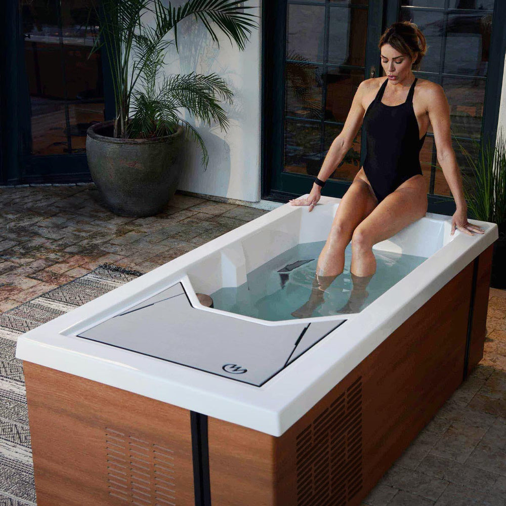 Woman sits on upper deck of cold tub and eases her legs in, visibly exhaling